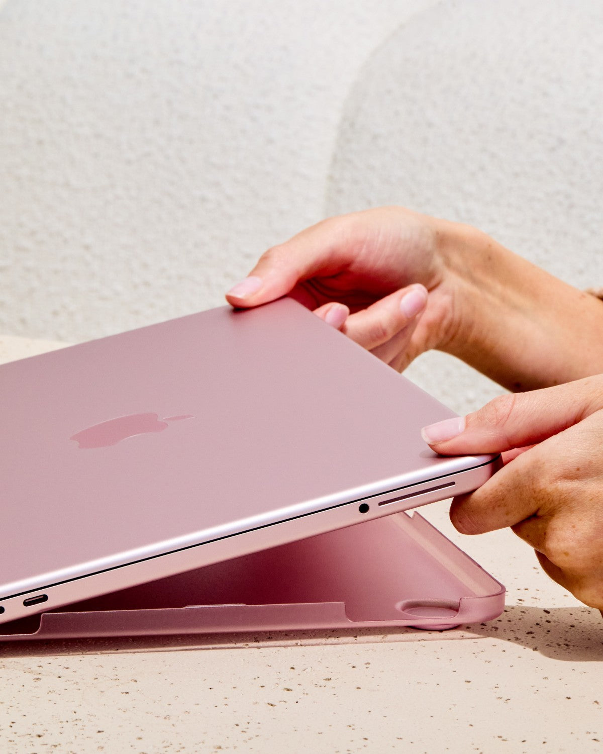 Hands installing the translucent Blush GhostShell Frost hardshell case bottom shell on a MacBook Neo.