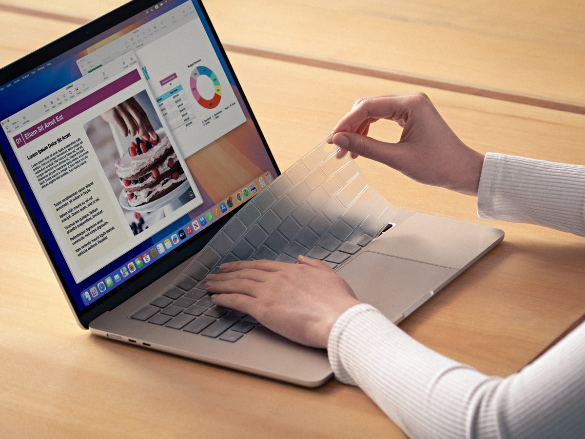 A person's hands are shown applying a clear GhostCover keyboard protector to a MacBook.