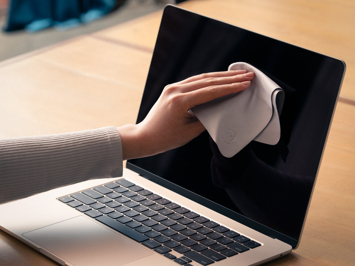 Hand wiping a MacBook screen with a gray GhostBlanket microfiber cloth