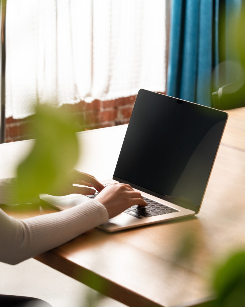 MacBook with GhostView privacy filter seen from the side in a sunlit room, content on the screen is not visible
