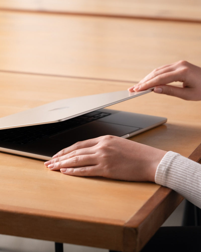 Hands closing a MacBook with the GhostView privacy filter still attached