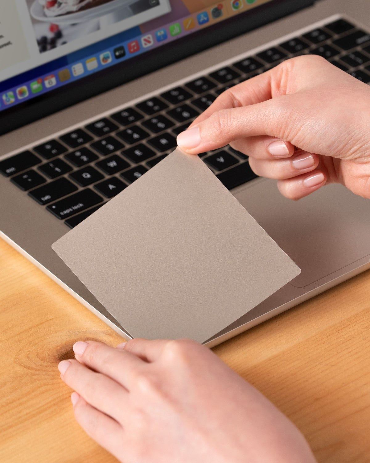Hand installing a GhostShield palm rest protector onto a MacBook