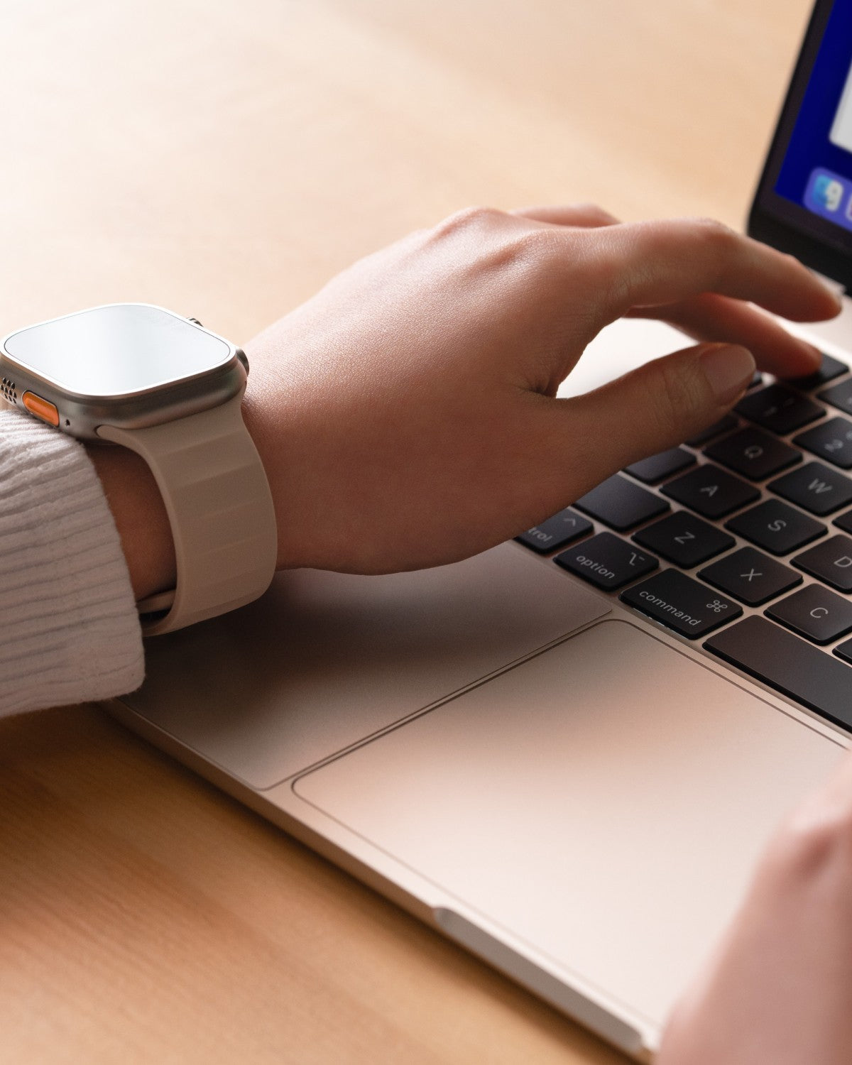 Hands typing on a MacBook while wearing a watch, with GhostShield protecting the palm rest